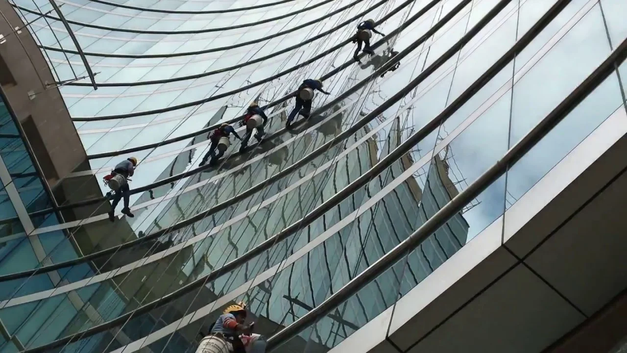 Imagem mostra uma equipe de pessoas limpando um predio de janelas espelhadas